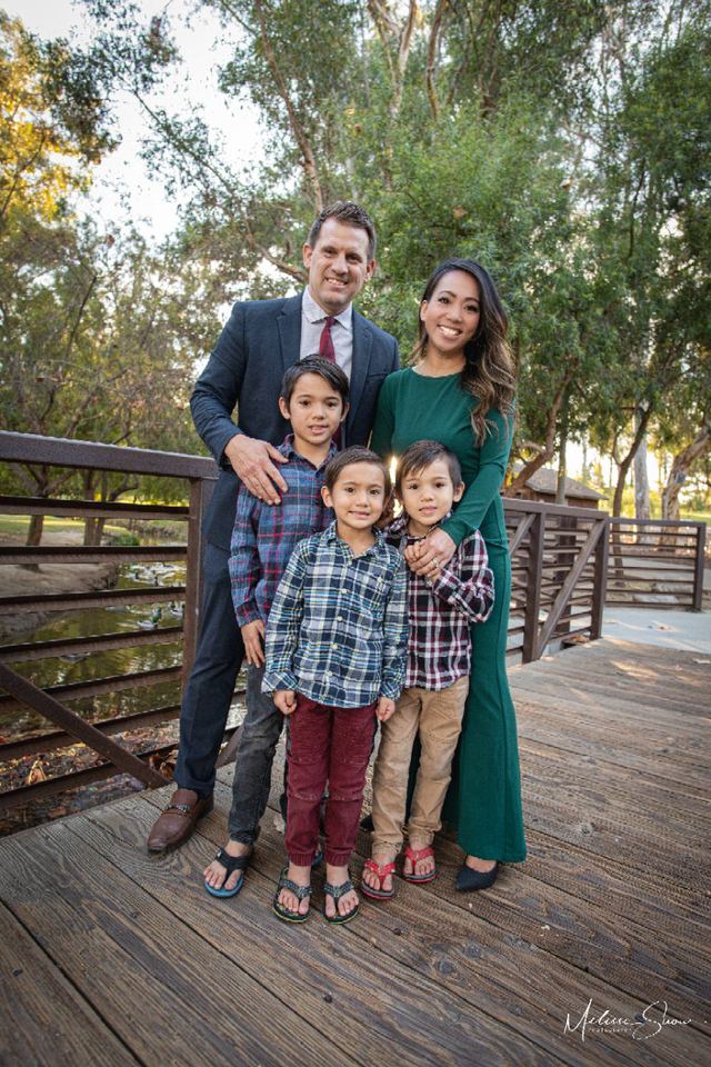 Amy Phan West with her husband and their three sons on a wooden footbridge in a park.
